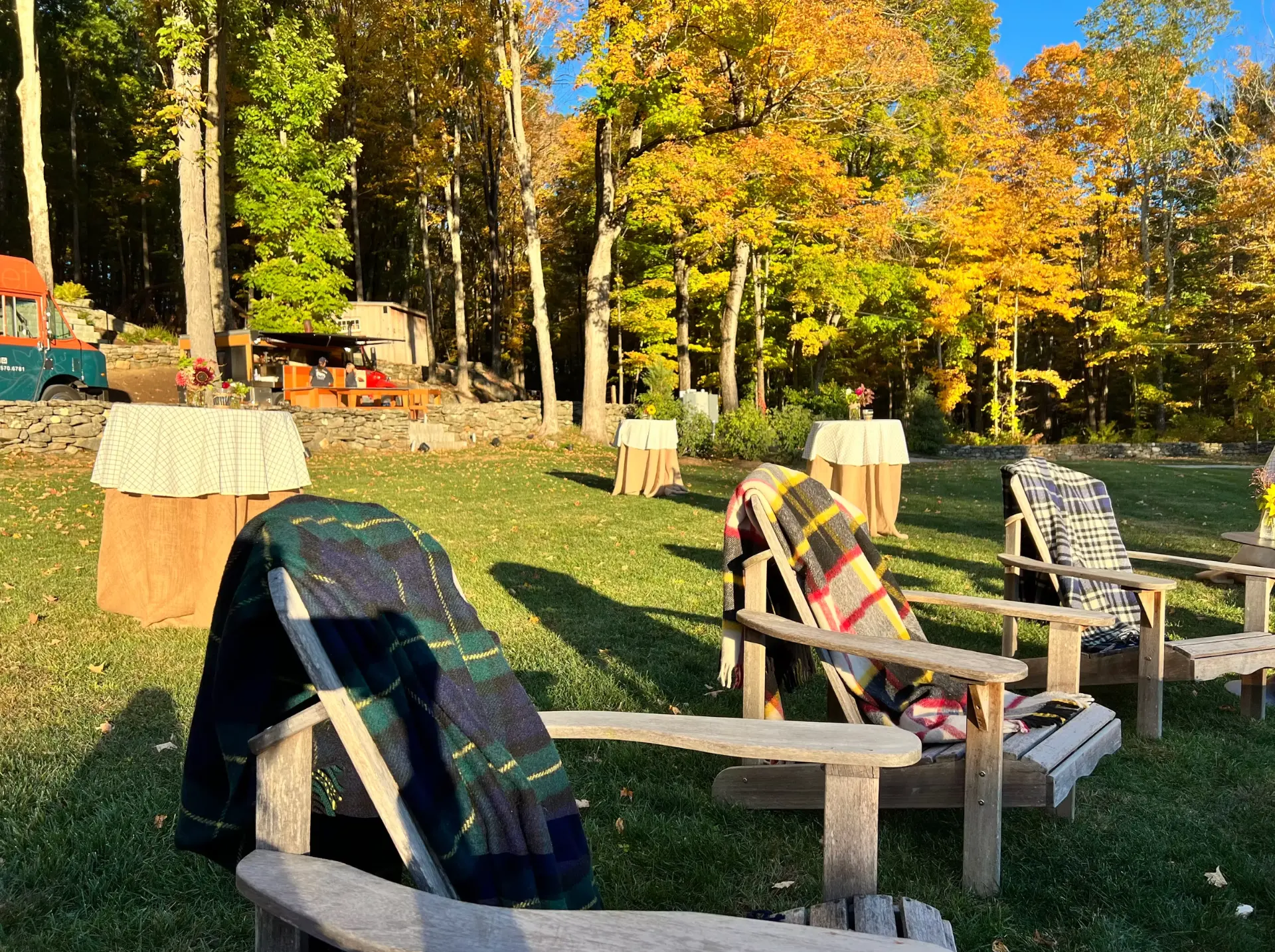 Wooden Adirondack chairs draped with plaid blankets on a lawn at an autumn gathering